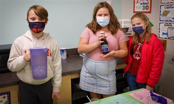 Students hold up science experiment supplies